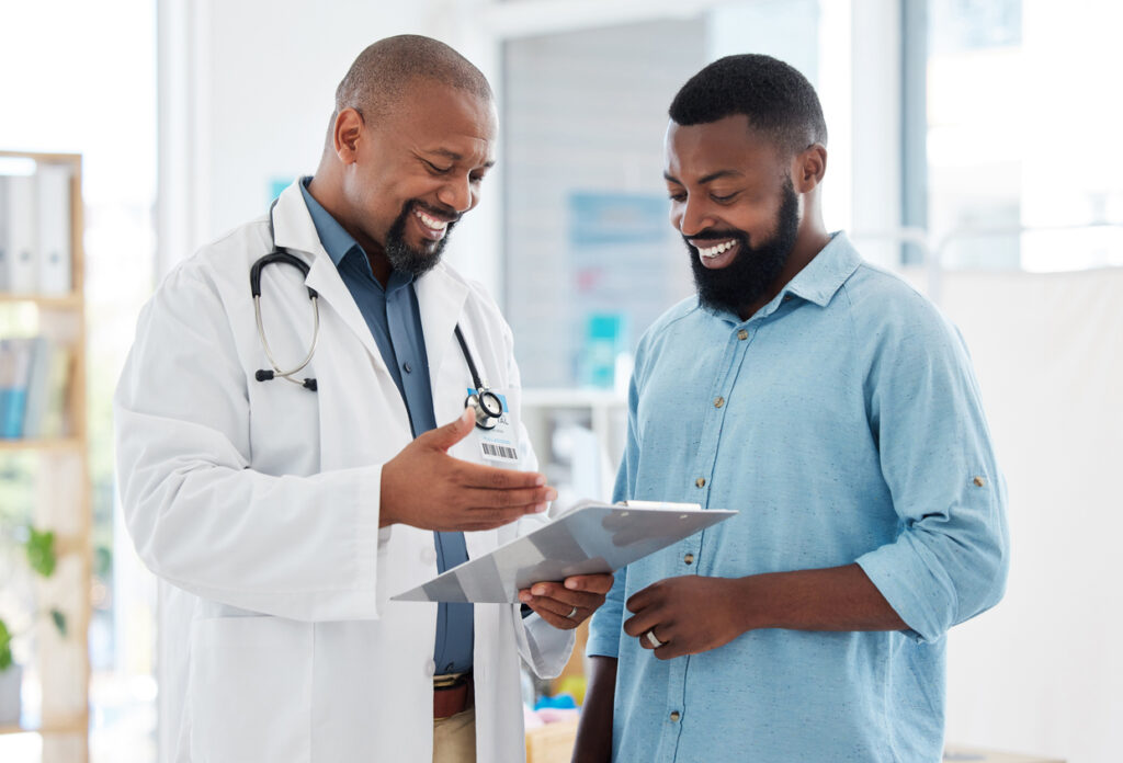 Young patient in a consult with his doctor. African american doctor showing a patient their results on a clipboard. Medical professional talking to his patient in a checkup